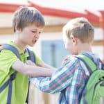 Boy picking a fight pushing another boy on school playground