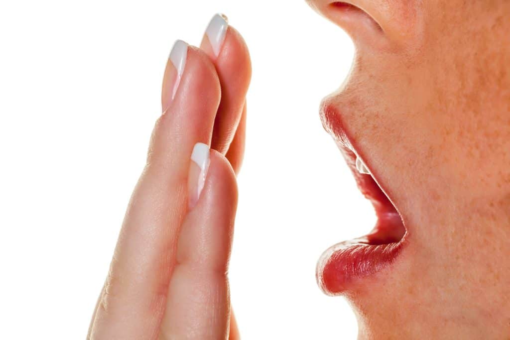 Closeup of woman with hand in front of open mouth checking for bad breath