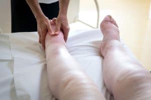 Massage therapist applying gentle lymphatic massage to a client’s leg with edema, demonstrating how massage can support clients with chronic illness and oncology care.